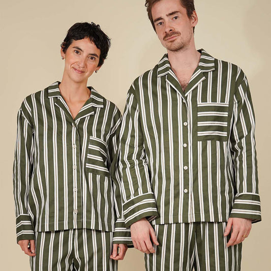A man and a woman modeling matching green and white vertically striped pajama sets against a solid beige background.